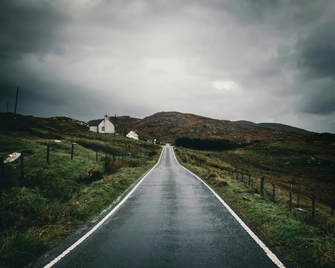 A single-track road on Barra running past a white house under heavy cloud