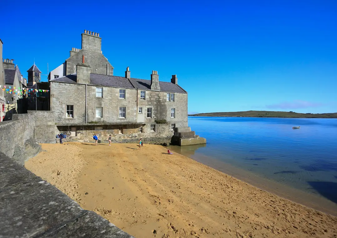 Grey stone houses of Lerwick above a sandy cove and still blue water