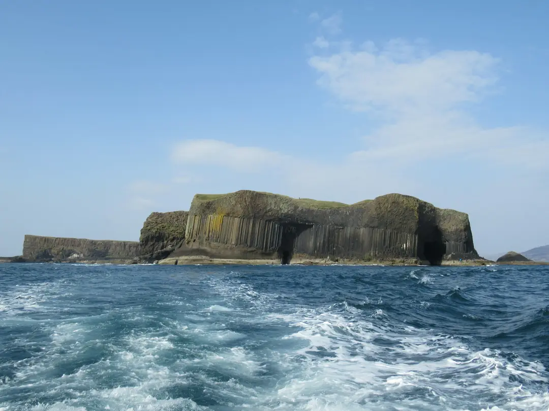 The basalt island of Staffa seen from a boat, its columns rising from a choppy sea